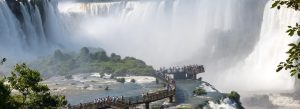 Tourists walking on viewing platform near Iguazu Falls surrounded by massive waterfalls and mist in Argentina