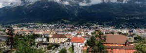 Panoramic view of Innsbruck, Austria, with colorful historic buildings, church towers, and the Alps rising dramatically in the background.