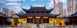 Traditional Chinese temple with red lanterns and yellow walls surrounded by modern city buildings China
