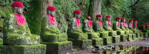 Moss-covered Jizo statues with red hats lining the Kanmangafuchi Abyss forest path in Nikko, Japan