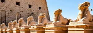 Row of ram-headed sphinx statues at Karnak Temple Complex in Luxor, Egypt under a bright blue sky.