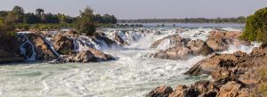 Panoramic view of Khone Phapheng Falls in Laos with powerful Mekong River rapids flowing over rocky terrain surrounded by tropical forest