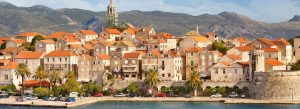 Panoramic view of Korčula Island, Croatia, featuring medieval stone buildings, terracotta rooftops, and the Adriatic coastline surrounded by mountains.