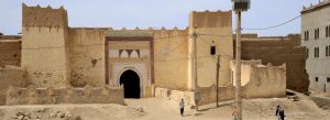 Traditional earthen walls and fortified entrance of Ksar Oulad Abdelhalim in Rissani, Morocco, surrounded by desert landscapes.