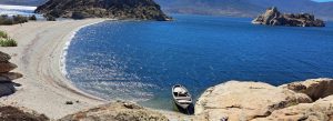 Beautiful sandy shoreline and blue waters of Lake Bafa in Turkey with a small boat resting beside rocky hills.