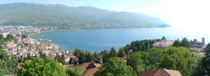 Panoramic view of Lake Ohrid with crystal-clear waters, red-roofed houses, and surrounding mountains in Albania.