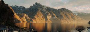 Golden sunset over Lake Traunsee in Austria with calm waters reflecting rugged mountain peaks.