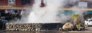 Steam rising from the natural Mae Kachan Hot Springs in northern Thailand, surrounded by stone walls and local shops in Chiang Rai Province.