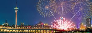 Night view of Macau Tower illuminated beside the city skyline with colorful fireworks lighting up the sky over Macau.