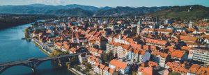 Aerial view of Maribor, Slovenia with red-roofed buildings, the Drava River, and surrounding hills in the background.
