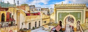 Historic entrance gate and traditional architecture in the Medina of Fez, Morocco, with people walking through the ancient city streets.