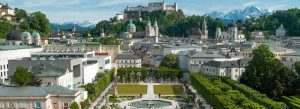 Panoramic view of Mirabell Gardens in Salzburg, Austria, with Hohensalzburg Fortress overlooking the historic city skyline and the Austrian Alps in the background.