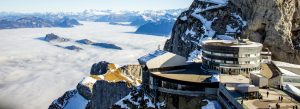 View from Mount Pilatus featuring snowy mountain peaks, clouds below, and panoramic terraces overlooking central Switzerland.