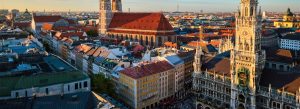 Aerial view of Munich, Germany, featuring Marienplatz, the New Town Hall clock tower, and the historic city center under warm evening light.