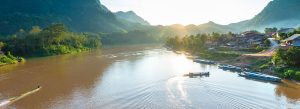 Sunset view over the Nam Ou River in Laos with longboats, riverside villages, and green mountain landscapes.
