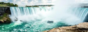 Panoramic daytime view of Horseshoe Falls with turquoise water, mist, and sightseeing boat near Niagara Falls.