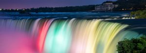 Illuminated Niagara Falls at night with colorful lights reflecting over cascading water and surrounding landscape.