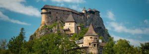 Oravský Hrad Castle perched on a rocky hill surrounded by lush green trees in northern Slovakia under a blue sky.