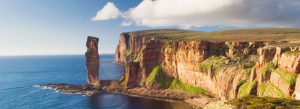 Dramatic sea cliffs and the famous Old Man of Hoy rock stack on the rugged coastline of the Orkney Islands in Scotland.