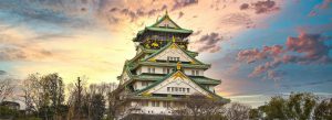 Osaka Castle illuminated by sunset skies in Osaka, Japan with traditional Japanese architecture.