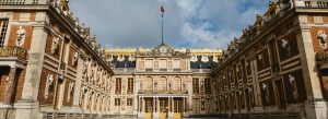Grand courtyard of the Palace of Versailles in France featuring ornate Baroque architecture and golden decorative details.