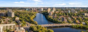 Panoramic aerial view of Ottawa skyline along the Rideau River with modern buildings, bridges, and lush green neighborhoods in Ontario, Canada.