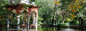 Elegant pavilion surrounded by lush gardens and a pond in Parque de María Luisa, Seville, Spain.