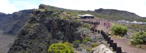 Panoramic view of Pas de Bellecombe volcanic lookout in Reunion Island with dramatic cliffs, hiking trails, and visitors overlooking the Piton de la Fournaise crater.
