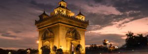 Patuxai Victory Monument illuminated at sunset in Vientiane, Laos with dramatic evening sky and city lights