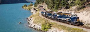 The Rocky Mountaineer luxury train traveling beside a turquoise lake through the Canadian Rockies.