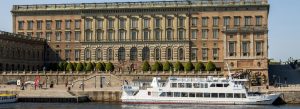 Royal Palace in Stockholm viewed from the waterfront with grand Baroque architecture and a sightseeing boat in the foreground.
