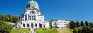 Front view of Saint Joseph’s Oratory of Mount Royal in Montreal, Canada, featuring its large green dome and grand staircase under a blue sky.