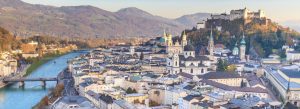 Panoramic view of Salzburg, Austria, featuring the Salzach River, historic old town, cathedral domes, and Hohensalzburg Fortress on the hilltop.
