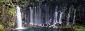 Shiraito Falls in Fujinomiya, Japan, featuring cascading streams of water flowing down moss-covered cliffs into a clear blue pool.