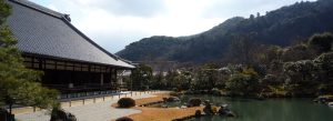 Sōgen Pond Garden at Tenryū-ji Temple in Kyoto, Japan, featuring a tranquil pond, traditional Zen landscaping, and temple buildings surrounded by forested hills.