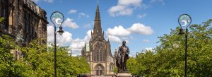 Front view of St. Mungo’s Cathedral in Glasgow with surrounding greenery and blue skies on a sunny day.