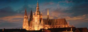 St. Vitus Cathedral illuminated at sunset in Prague, Czech Republic, featuring Gothic architecture and towering spires above the historic city skyline.
