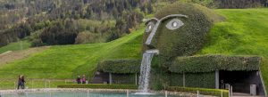 The Giant at Swarovski Kristallwelten in Wattens, Austria, featuring a grassy face sculpture with a waterfall flowing from its mouth surrounded by green hills.