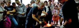 Visitors watching a traditional sword-making demonstration in a blacksmith workshop in Toledo, Spain, as glowing metal is forged by hand.
