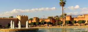 Historic fortified walls and fountains in the city of Taroudant, Morocco, surrounded by palm trees and clear skies.