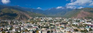 Panoramic view of Thimphu city in Bhutan surrounded by lush green Himalayan mountains under a bright blue sky.