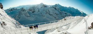 Tourists walking across the Titlis Cliff Walk suspension bridge surrounded by snow-covered Swiss Alps in Engelberg, Switzerland.