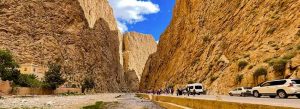 Visitors walking and driving through the dramatic rock walls of Todra Gorge in Morocco under a bright blue sky.