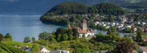 Panoramic view of Spiez Castle overlooking Lake Thun with lush green hills and charming Swiss village scenery in Switzerland.
