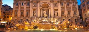 The illuminated Trevi Fountain in Rome, Italy featuring baroque sculptures and flowing water at night.