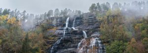 Tvindefossen Waterfall cascading down rocky cliffs surrounded by misty forest landscape in Norway.