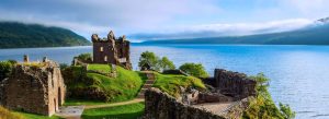 Ancient stone castle ruins overlooking a scenic lake surrounded by green hills in the Scottish Highlands.