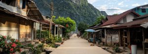 Traditional village street in Muang Ngoi Neua, northern Laos, surrounded by lush limestone mountains and wooden houses.