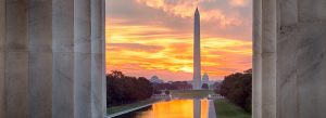 View of the Washington Monument and Reflecting Pool at sunset, framed by the columns of the Lincoln Memorial in Washington, D.C.
