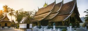 Sunset view of Wat Xieng Thong featuring traditional Lao temple architecture and palm trees in Luang Prabang